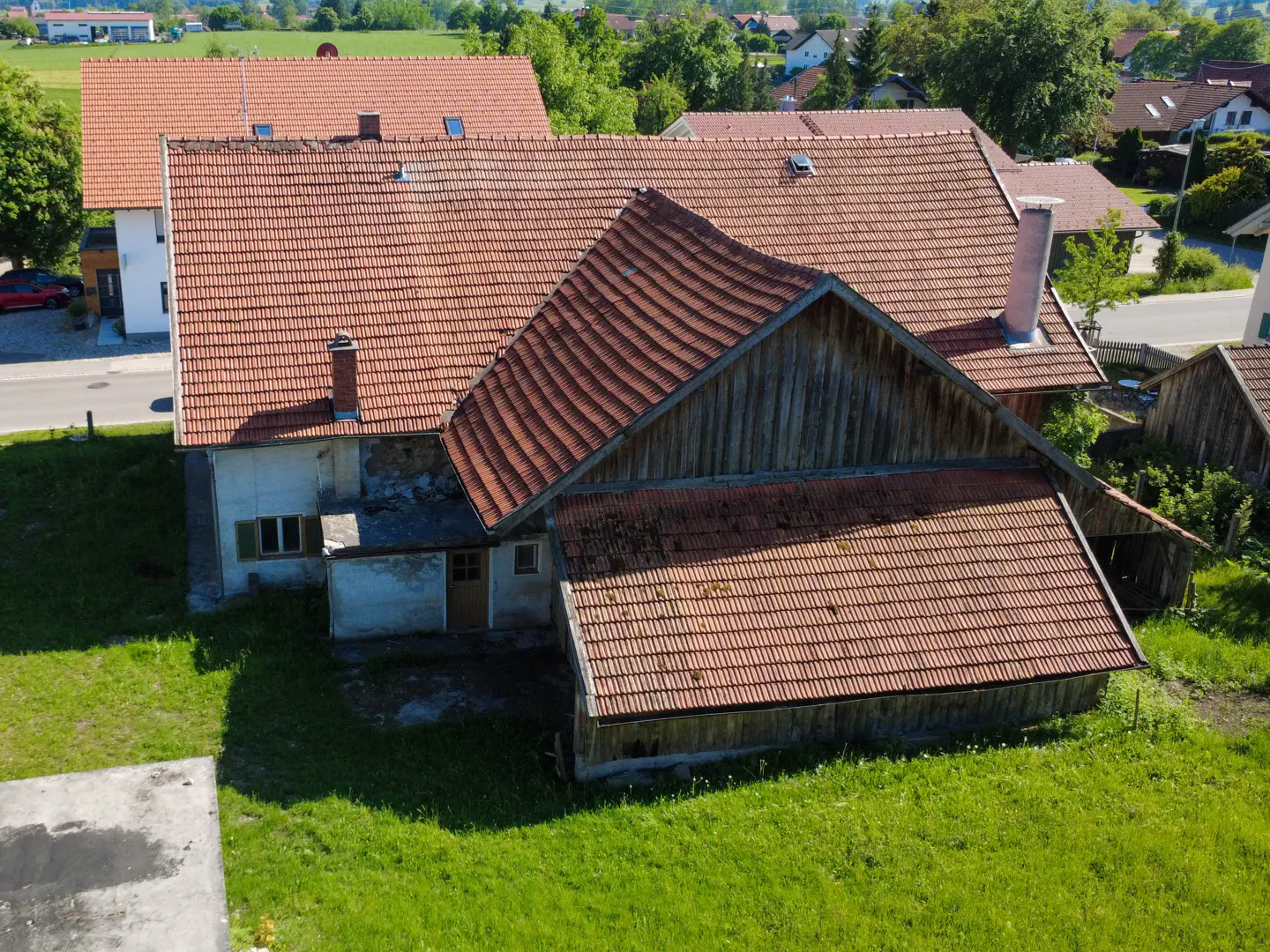 Aerial view of a large, rustic house with a red tile roof, surrounded by green grass and trees.