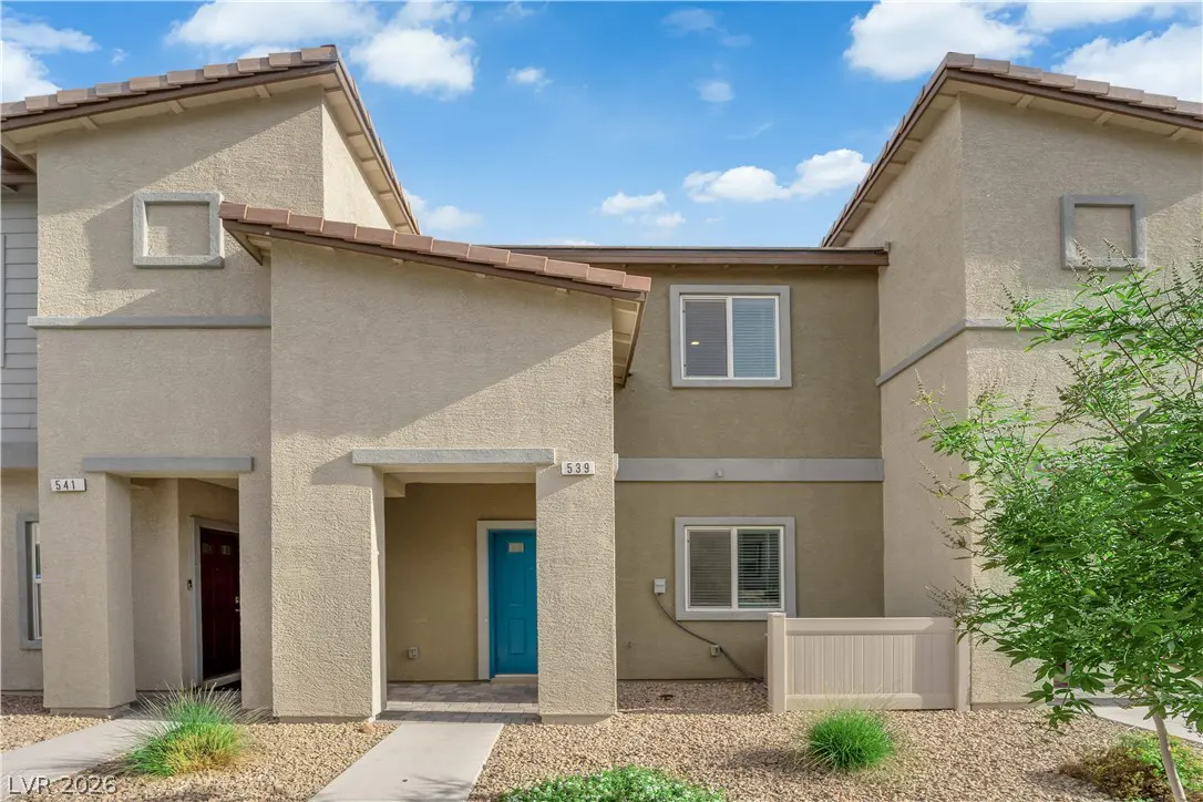 Two-story tan townhouses with brown roofs, blue door at 539, red door at 541, and blue sky.