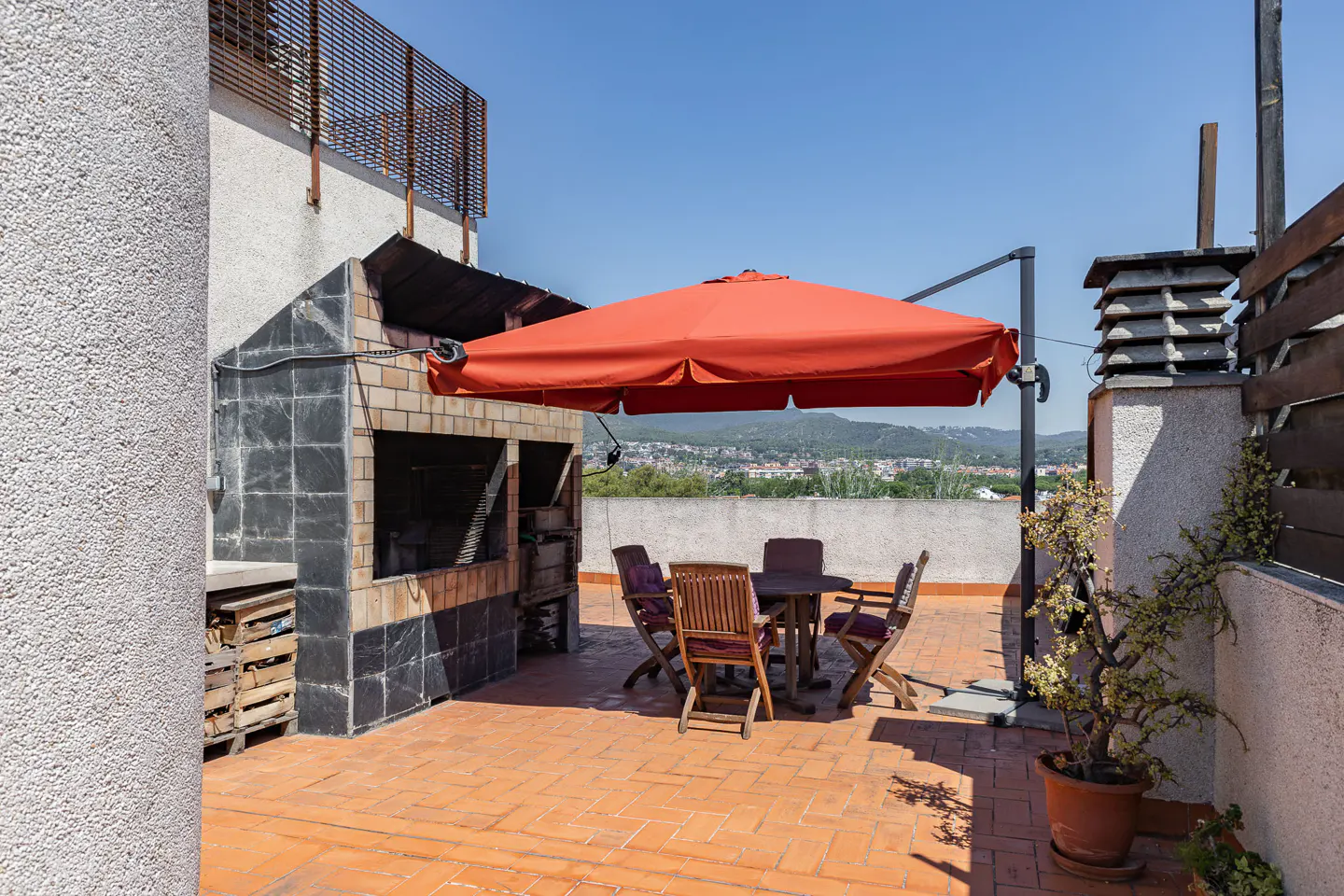 Rooftop patio with brick flooring, a built-in grill, a round table with chairs, and a large orange umbrella.