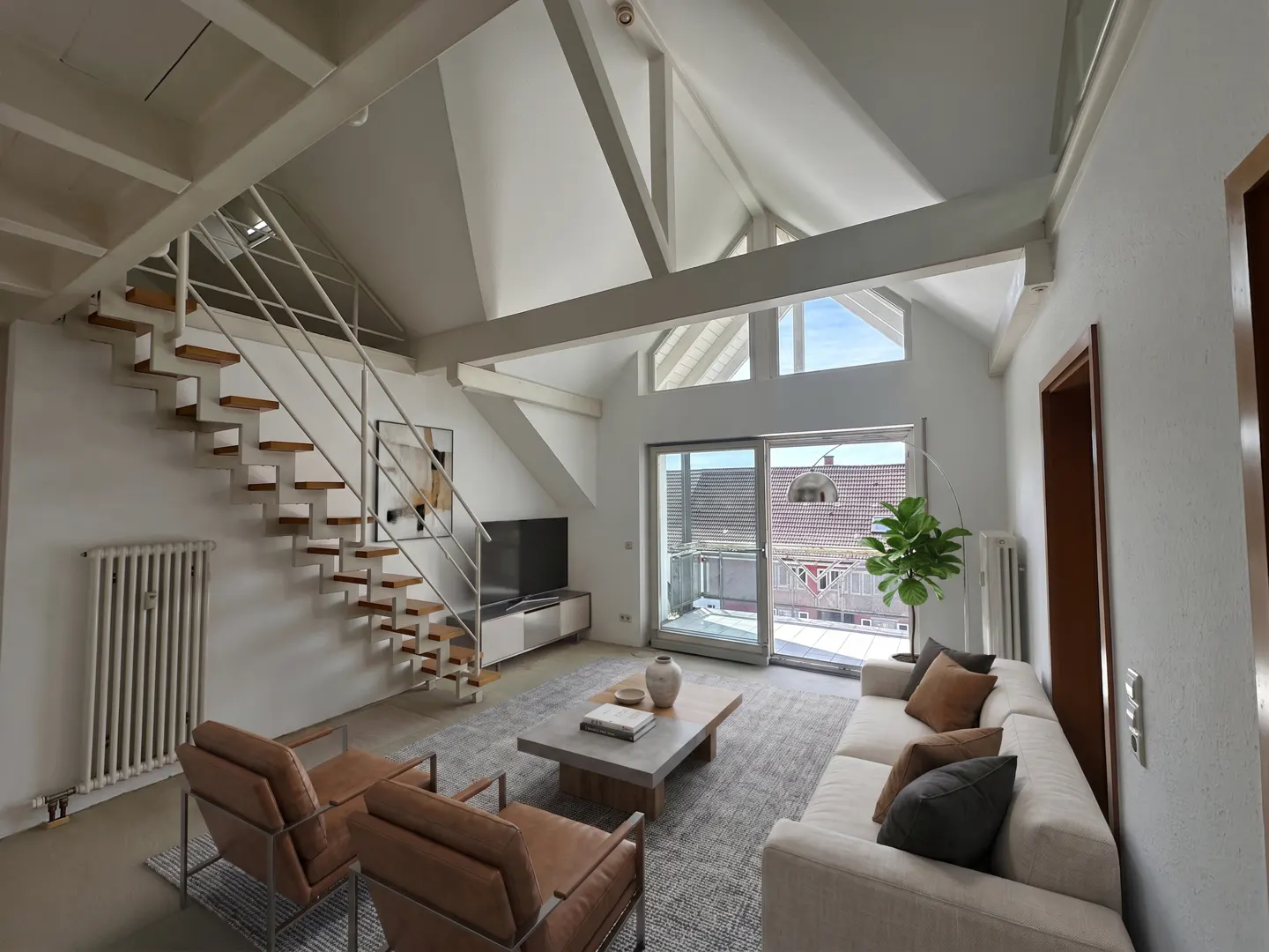 Modern living room with vaulted ceilings, floating staircase, leather armchairs, sofa, and balcony access.
