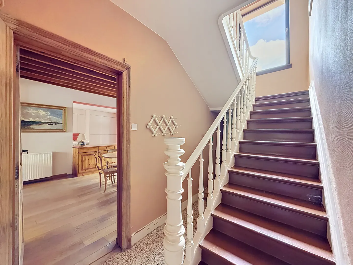 Staircase with dark wood steps and white railings in a peach-colored hallway, leading to a view of a dining room.