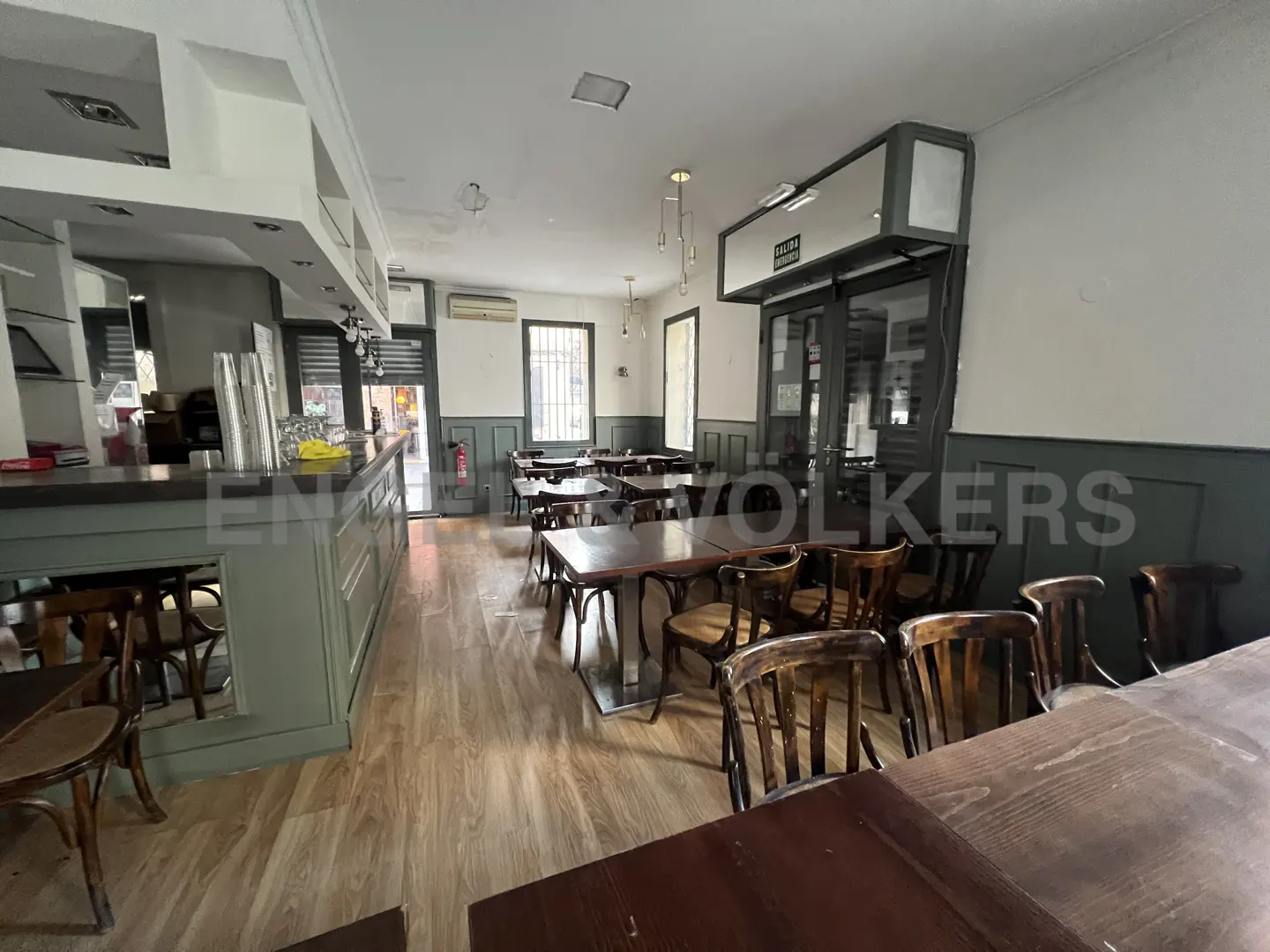 Empty restaurant interior with wooden tables and chairs, a bar area, and light wood floors.