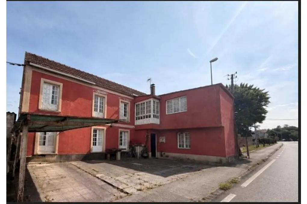 Exterior view of a two-story red house with white windows and a covered parking area on a sunny day.