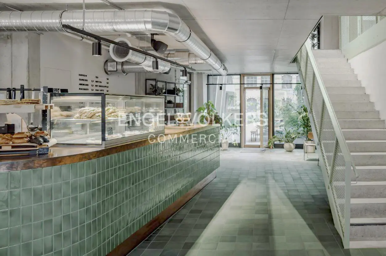 Interior view of a commercial space with a green tiled counter, display case, and stairs.