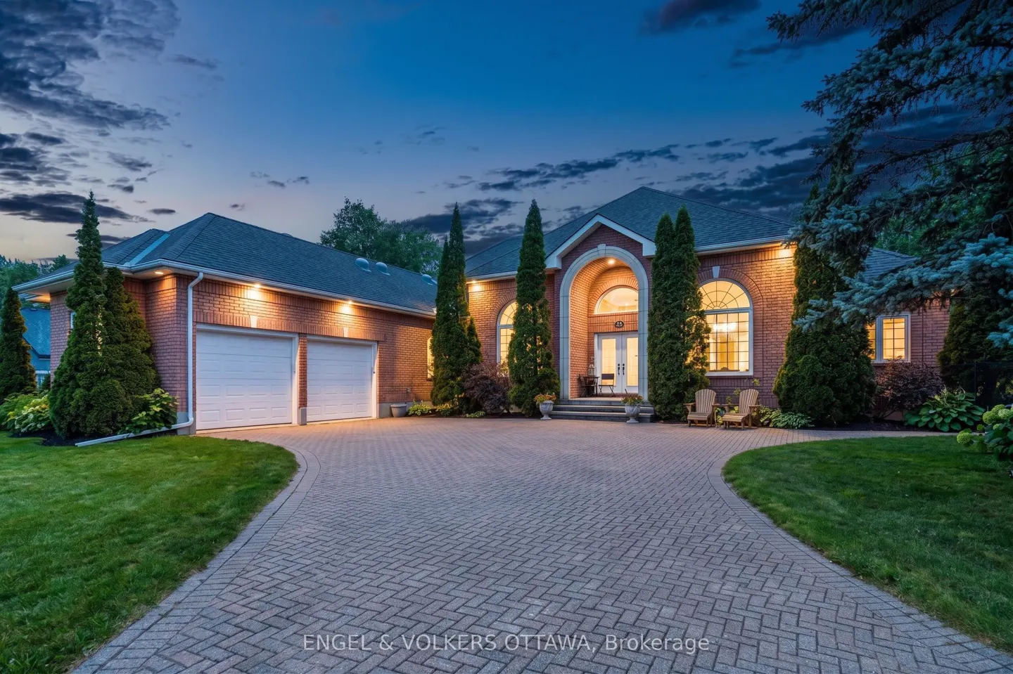Exterior shot of a red brick house with a large driveway and a two-car garage at dusk.