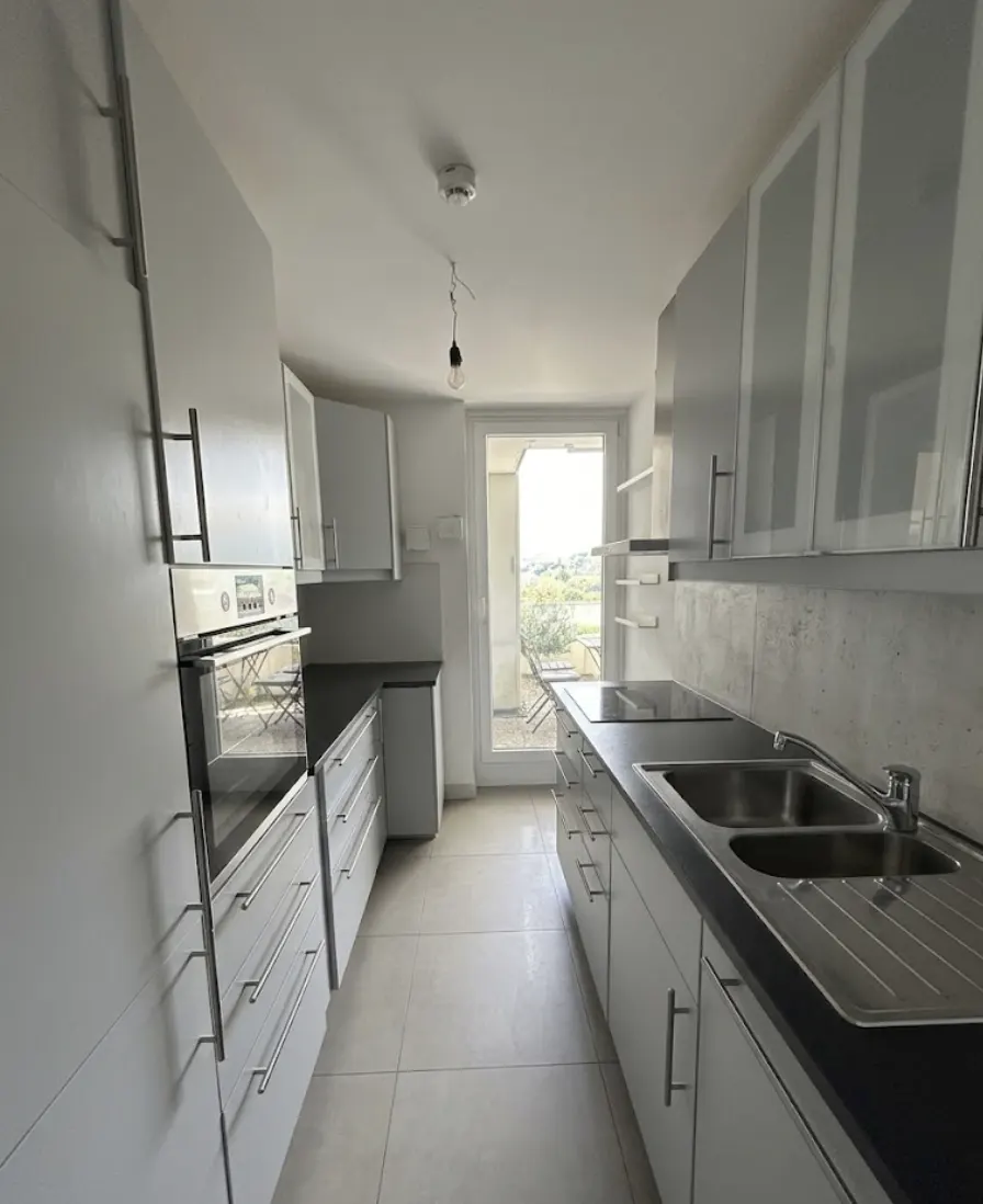 A bright, modern kitchen with white cabinets, stainless steel appliances, and a door leading to a balcony.