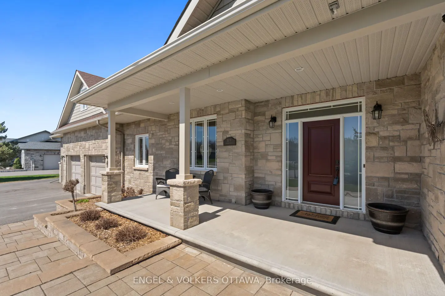 Stone house exterior with a covered porch, chairs, and a dark wood front door with sidelights. Planters flank the entrance.