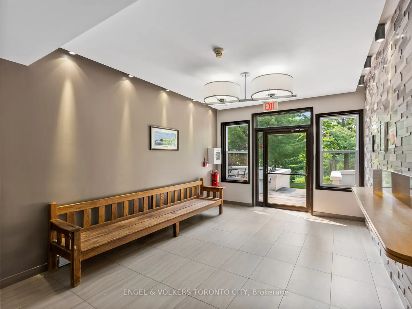 Lobby with a wooden bench, tiled floor, and an exit door leading to a green outdoor area. A textured wall adds visual interest.