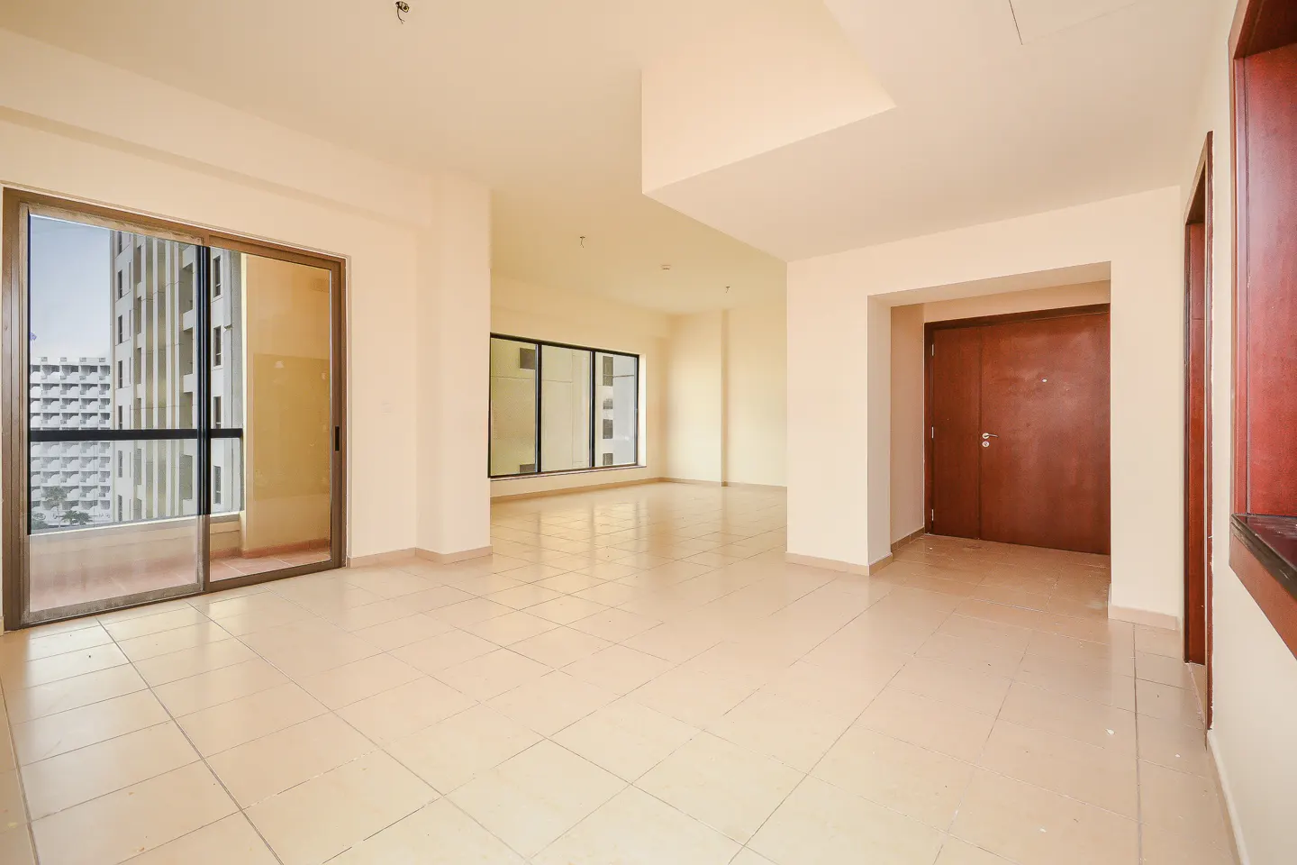 Unfurnished room with beige tile floor, cream walls, and a sliding glass door to a balcony with a city view. Brown double doors are visible.