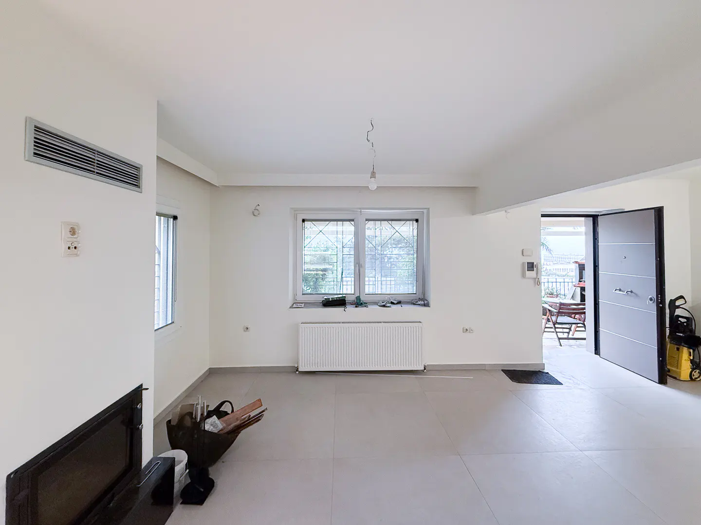 Bright, empty room with white walls, gray floors, and a window. A door leads to a patio with furniture.