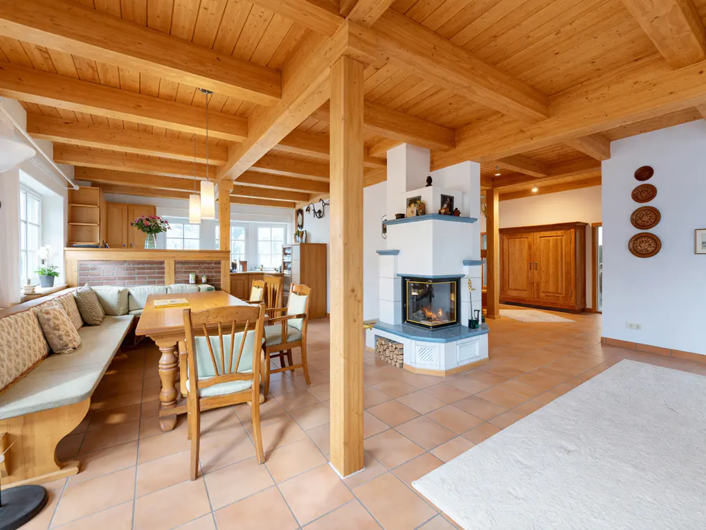 Open-concept living space with wood beams, tile floors, and a white fireplace with blue accents. A dining table and built-in bench are visible.