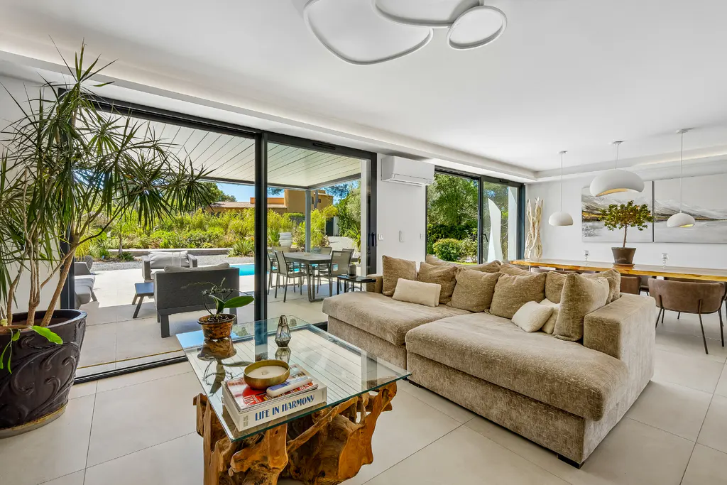 Bright living room with a beige sectional sofa, glass coffee table, and sliding glass doors to a patio with a pool.