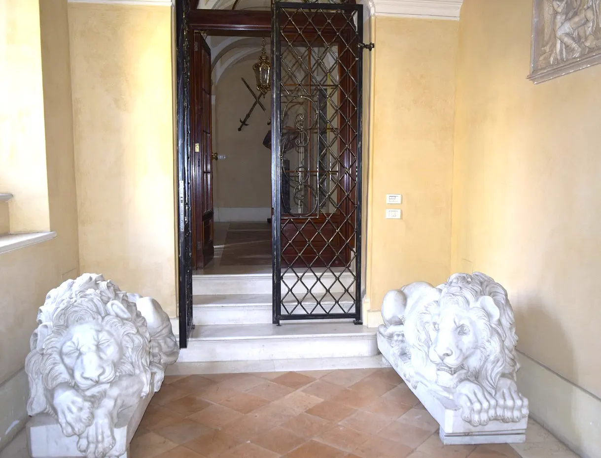 Interior view of a hallway with two lion statues, a metal gate, and an open wooden door.