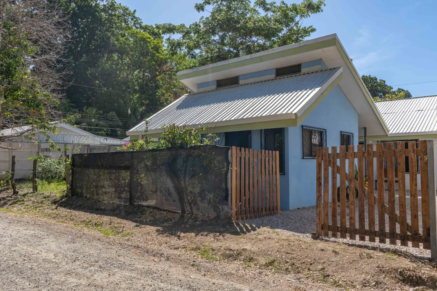 Exterior view of a light blue house with a metal roof and a wooden fence.