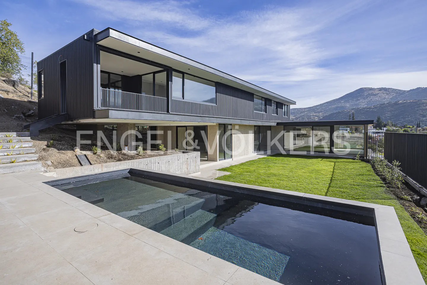 Modern two-story black home with a rectangular swimming pool, green lawn, and mountain views under a clear blue sky.