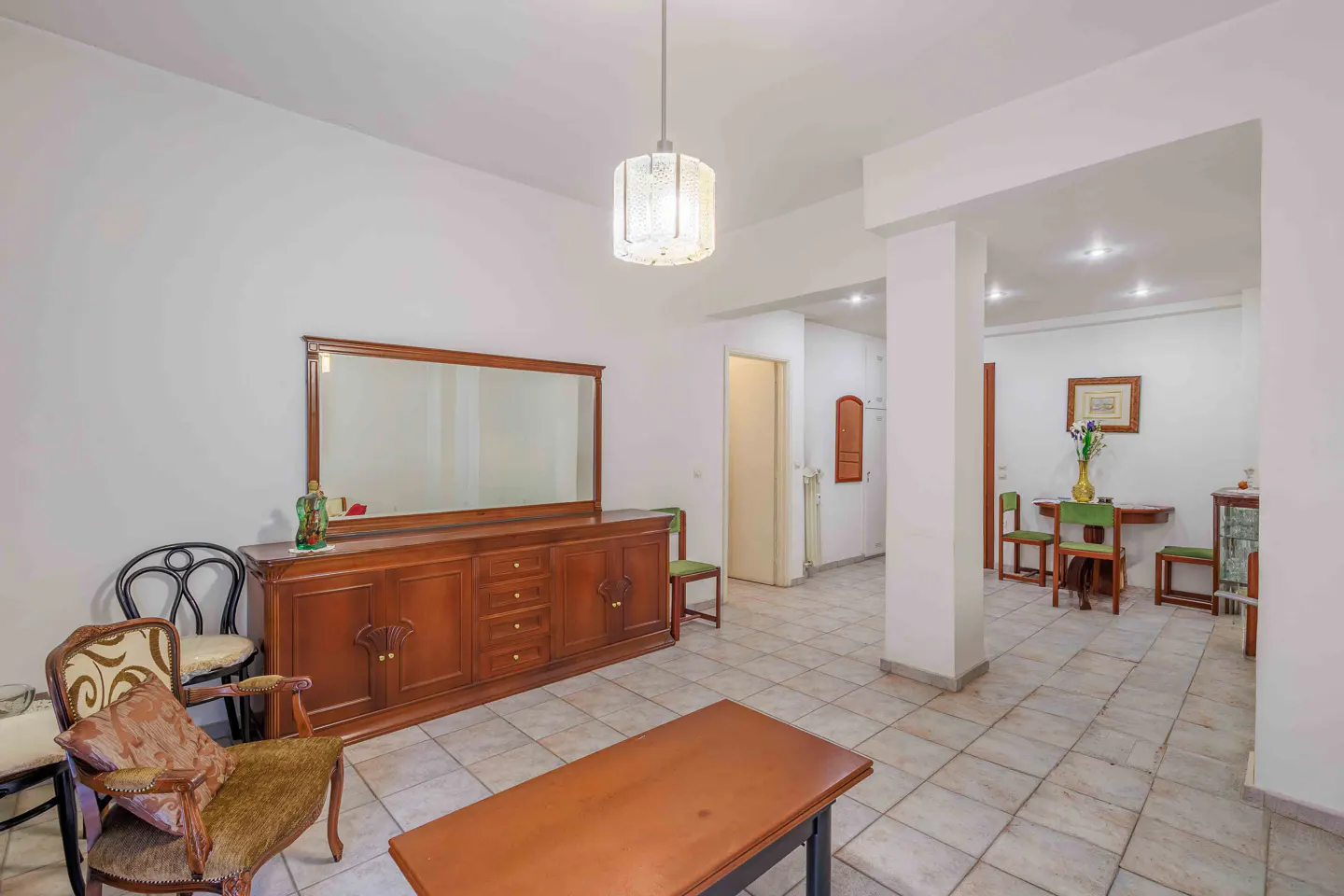 A living room with a brown wooden dresser, mirror, chairs, and a table on a tiled floor.