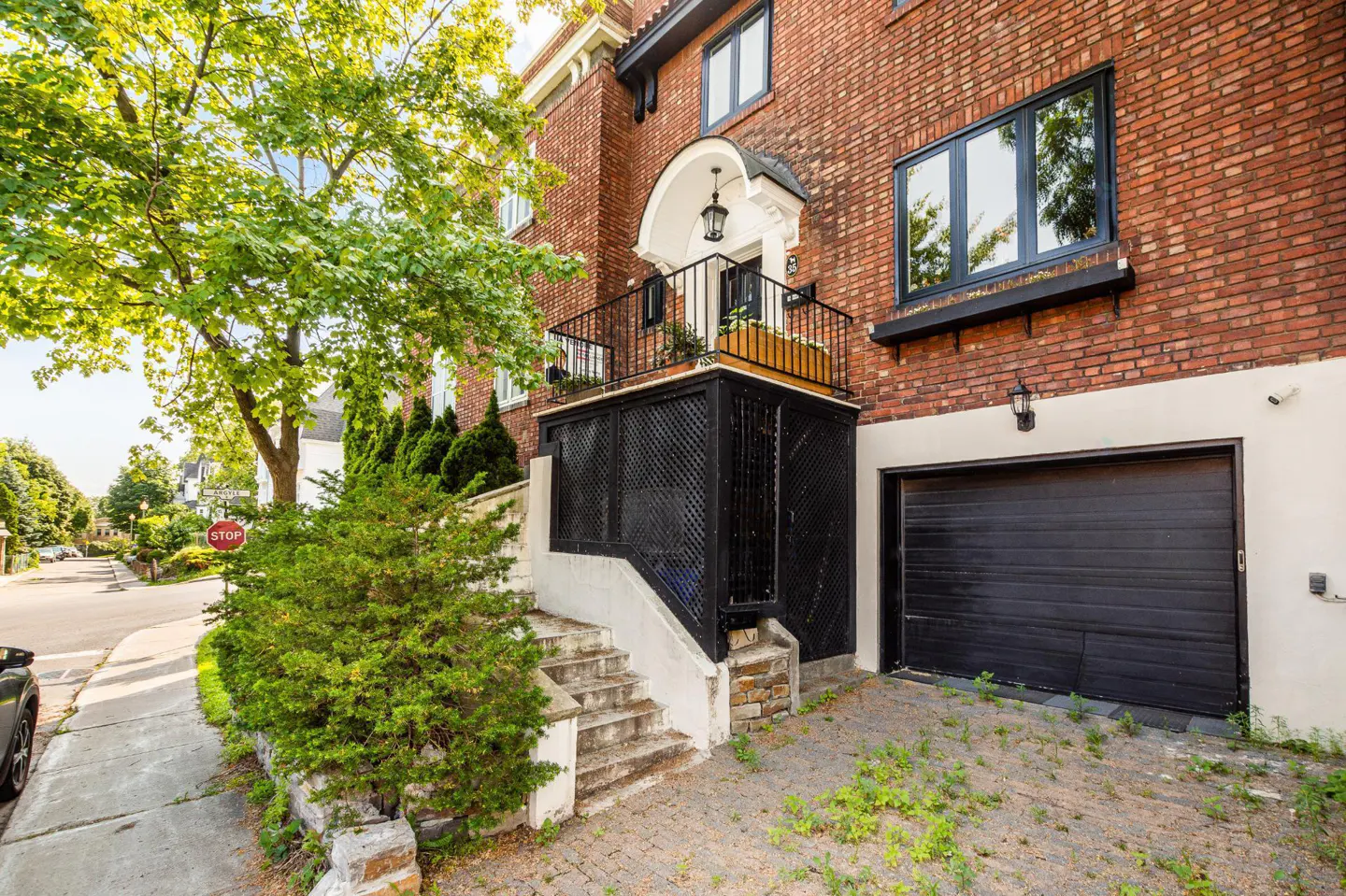 Brick house with black garage door and lattice-covered porch. Stone steps lead to the porch. A tree is on the left.
