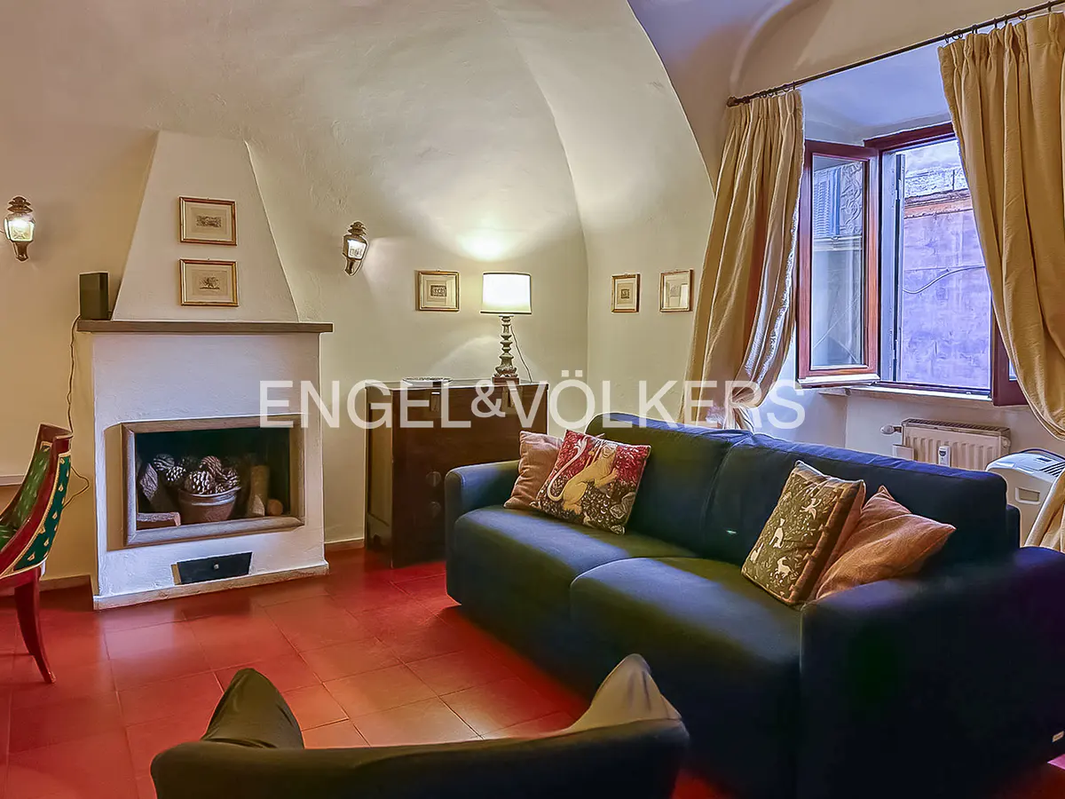 Living room with red tile floor, fireplace, and blue sofa with decorative pillows. Curtains frame a window.