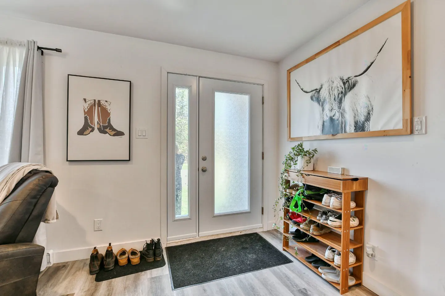 Entryway with white walls, a shoe rack, and a white door with frosted glass. Artwork of a cow and boots adorn the walls.