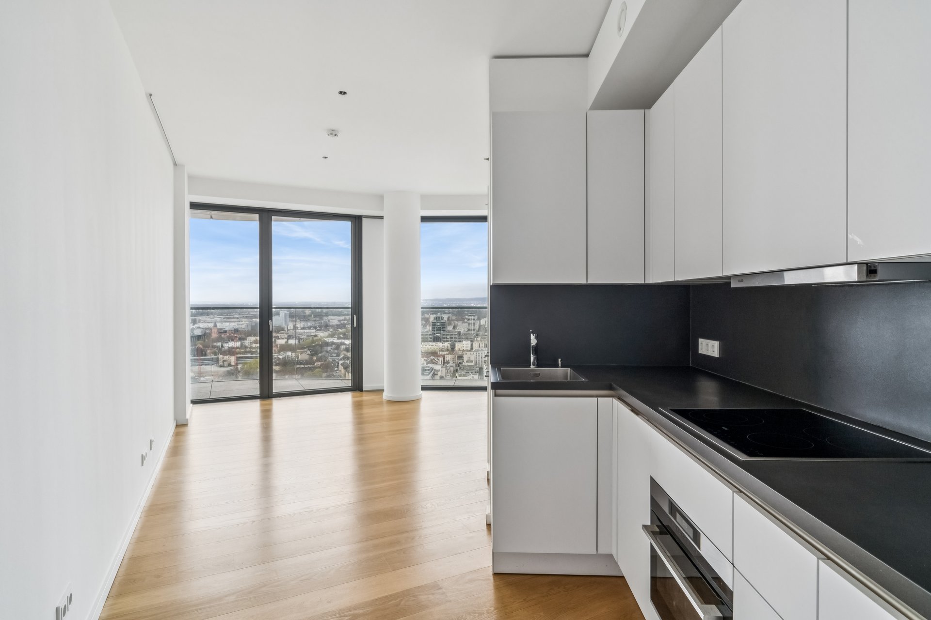 Modern kitchen with white cabinets, black countertops, and hardwood floors, featuring floor-to-ceiling city view windows. [AI-generated text]