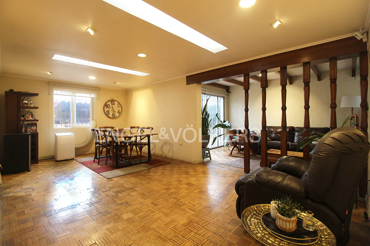 A living and dining area with parquet floors, a dining table, and a brown leather recliner. A wooden beam separates the spaces.
