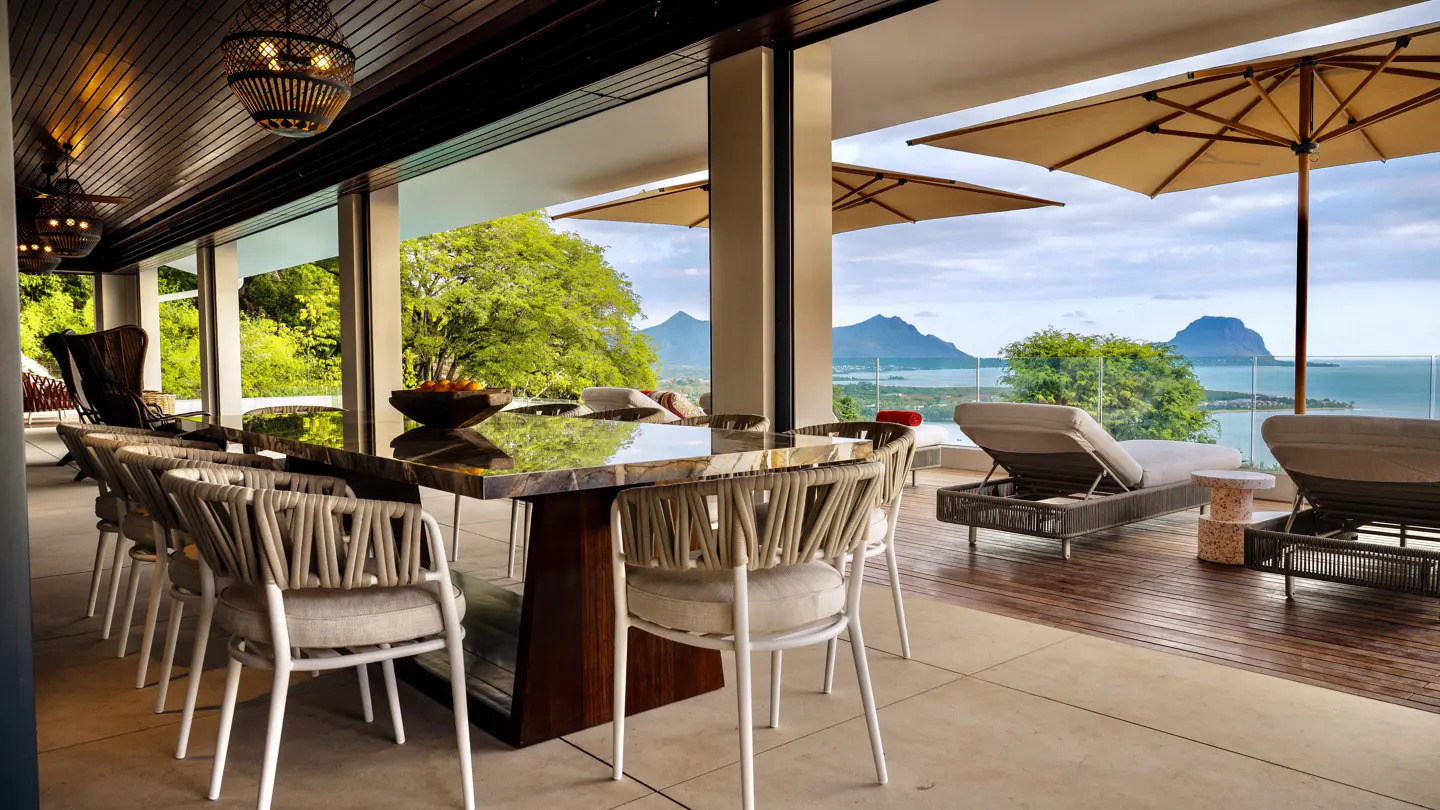 Outdoor dining area with a marble table, rope chairs, and ocean views. Lounge chairs and umbrellas are on the deck.