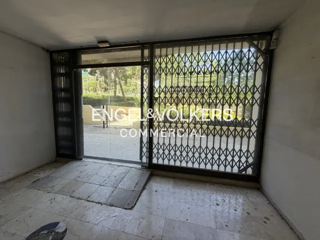 Empty commercial space with marble floors, a glass door, and a metal security gate looking out onto a sunny street.