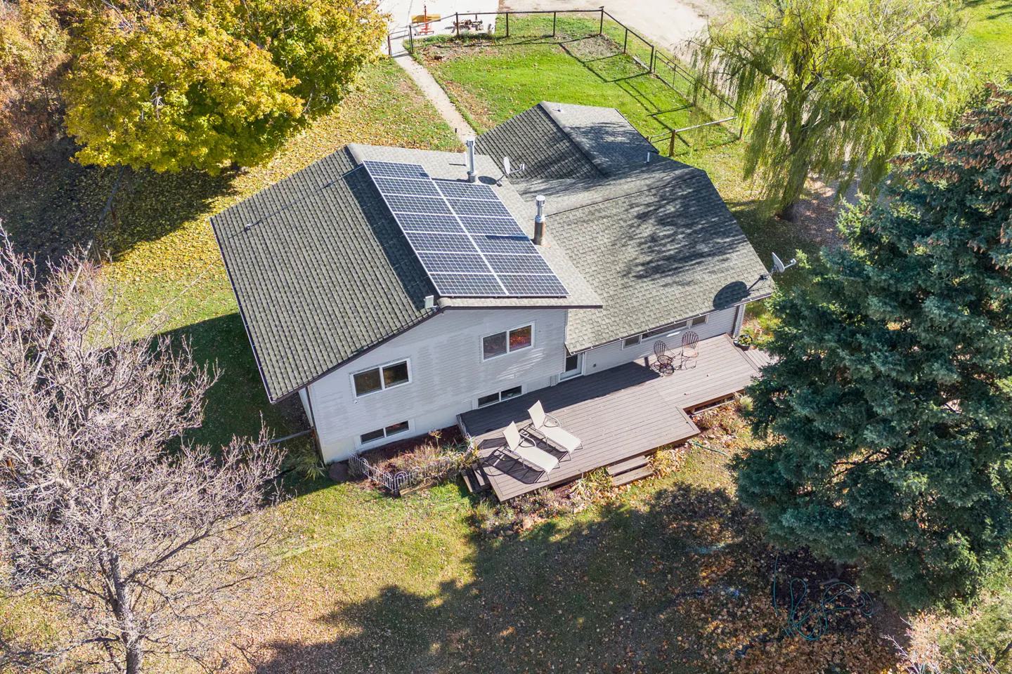 Aerial view of a light gray house with solar panels on the roof and a wooden deck with lounge chairs.