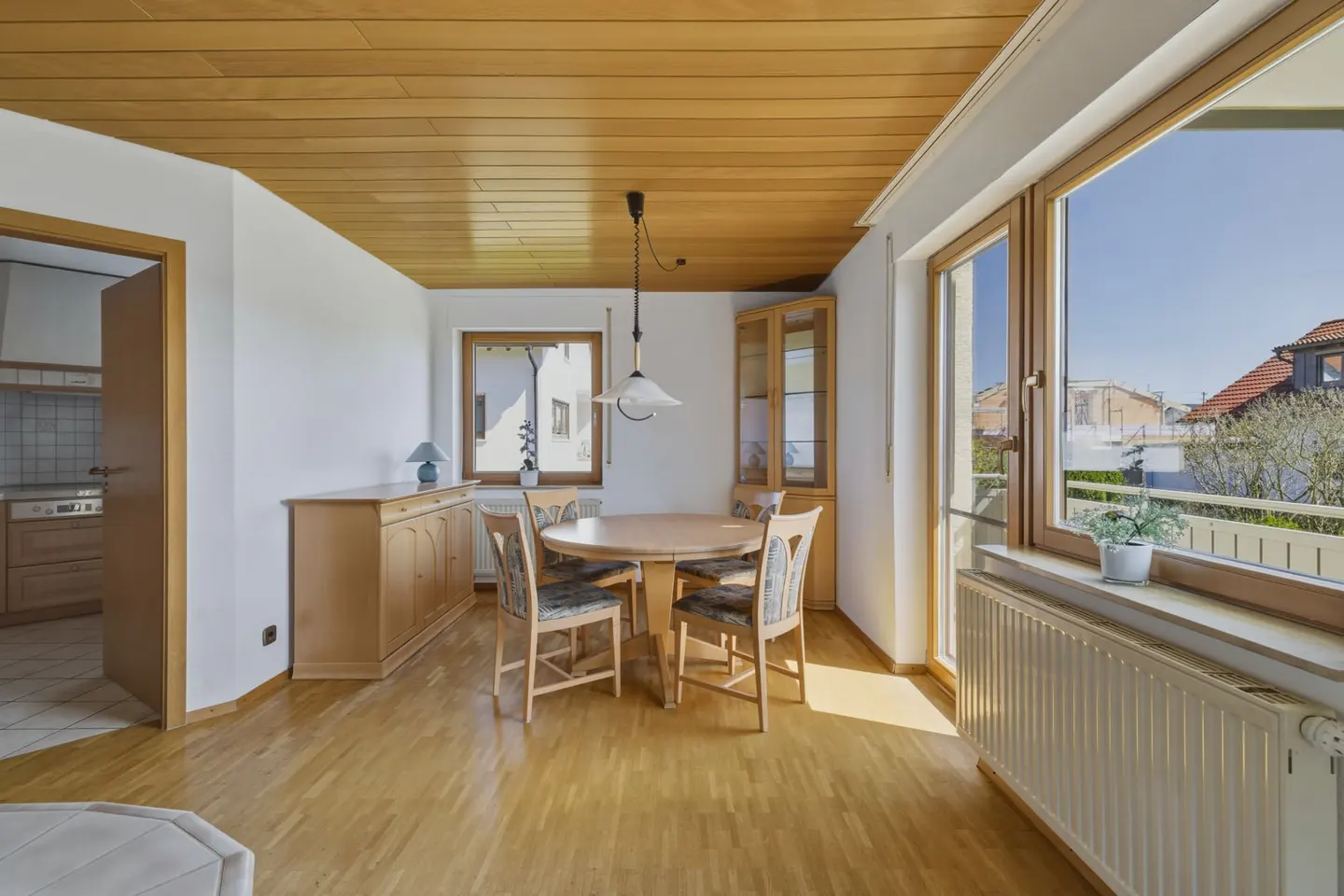 Bright dining room with wood floors, ceiling, and trim. A round table with four chairs sits near a large window with a view.