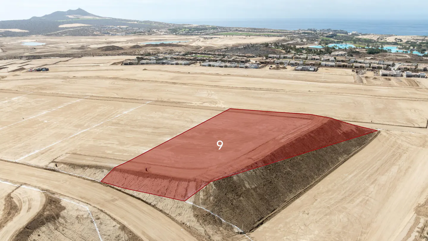 Aerial view of a vacant, graded land plot marked with a red overlay and the number 9, set in a coastal desert landscape.