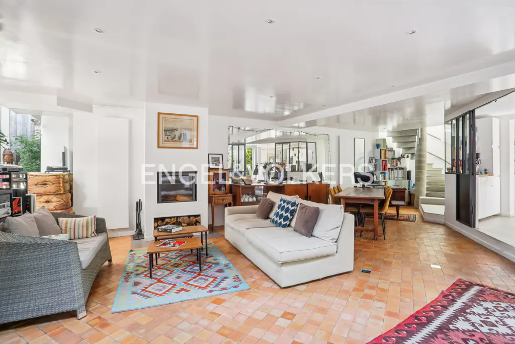 Bright living room with terracotta tile floor, white walls, fireplace, sofas, and dining area with a spiral staircase in the background.