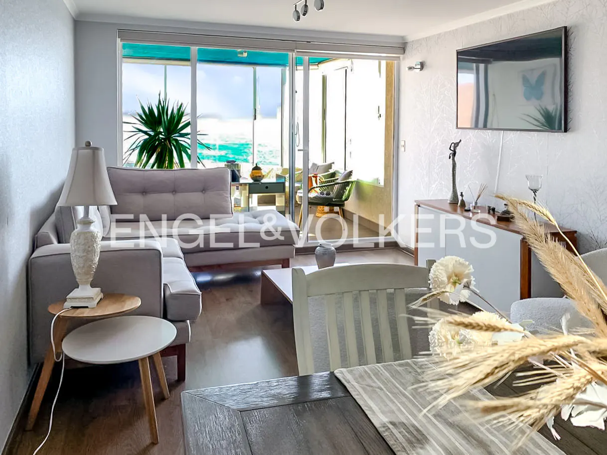 Living room with gray sofa, wood floors, and sliding glass doors to a balcony with ocean views. TV on the wall.