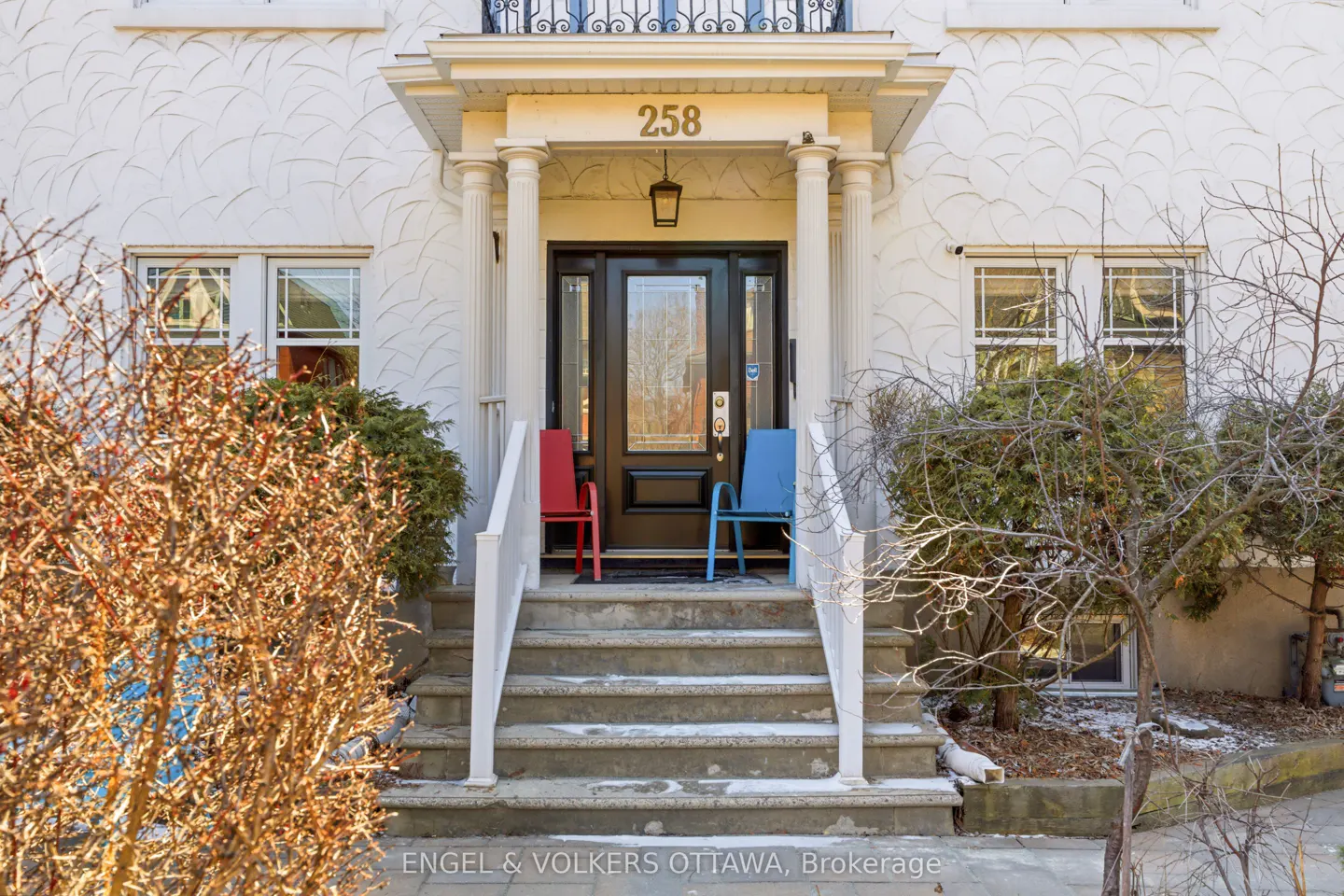 Front exterior of a white house with a black door, number 258 above, and red and blue chairs on the porch.