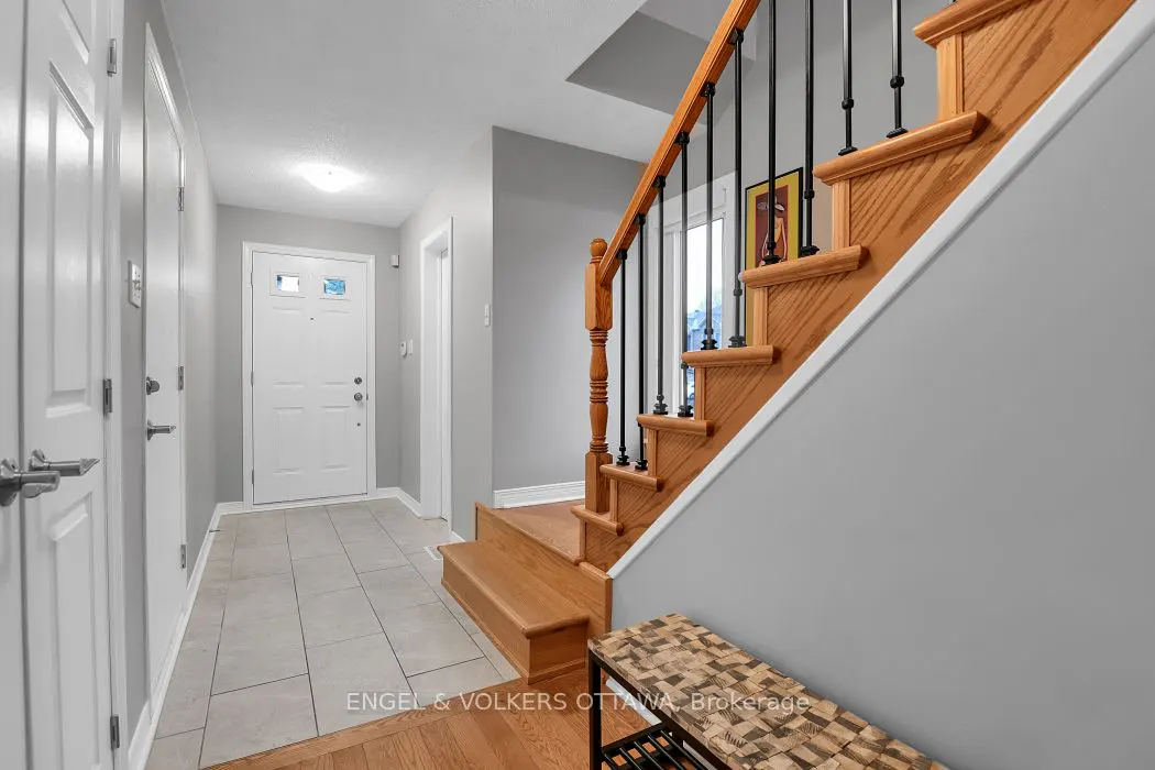 Entryway with white door, tile floor, and oak stairs with black railings. Gray walls and white trim.