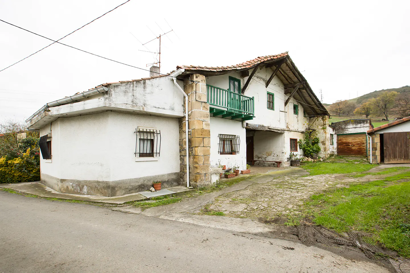 Exterior view of a two-story white house with a green balcony and a red tile roof. A stone pathway leads to the house.