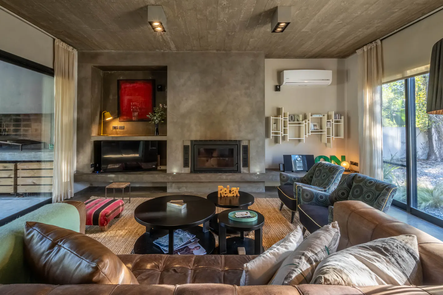 Living room with a brown leather sofa, armchairs, and a fireplace. The walls are gray and there are large windows with white curtains.