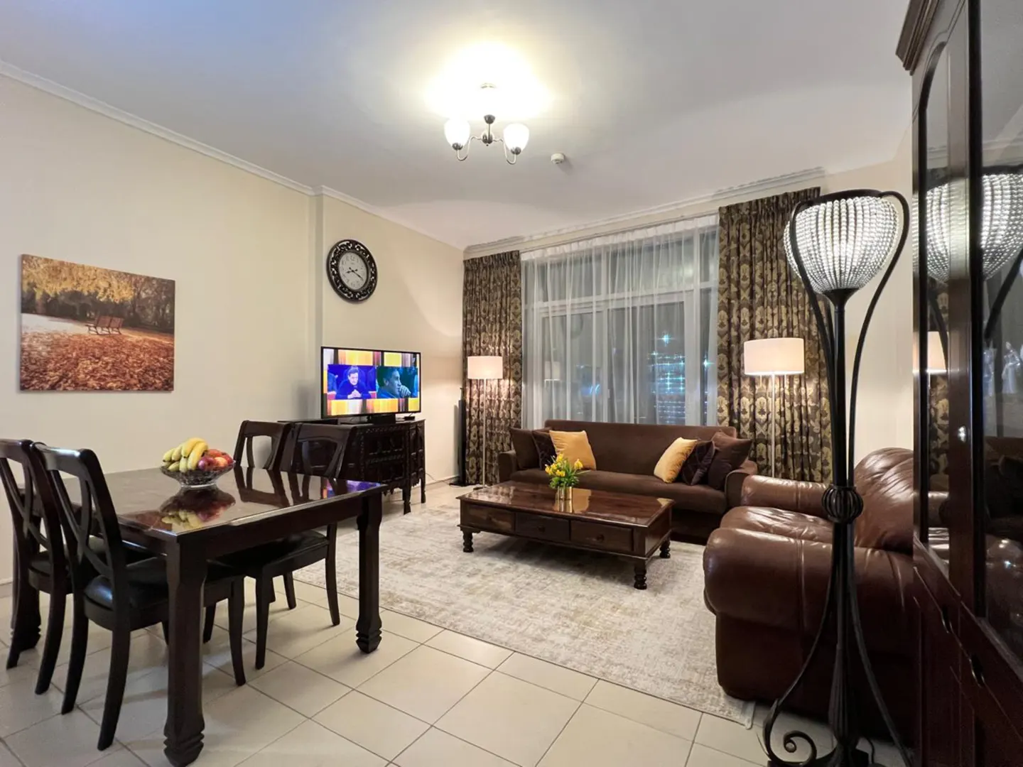 Living room and dining area with dark wood furniture, brown sofas, TV, and a fruit bowl on the dining table.