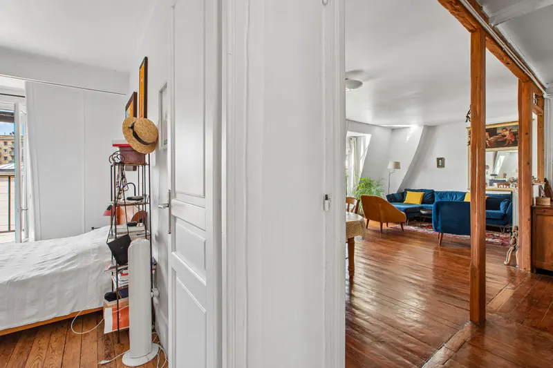View from a bedroom into a living room with hardwood floors, a blue sofa, and a yellow armchair.