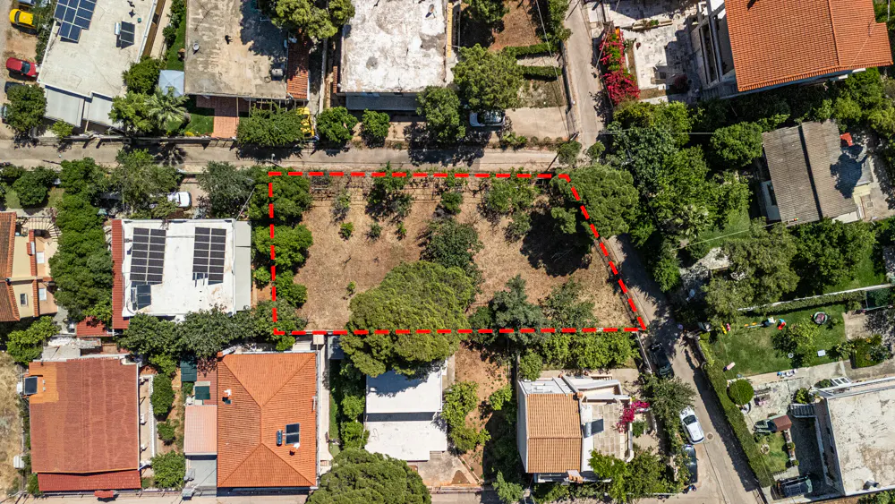 Aerial view of a vacant rectangular plot of land outlined in red, surrounded by residential houses and trees.