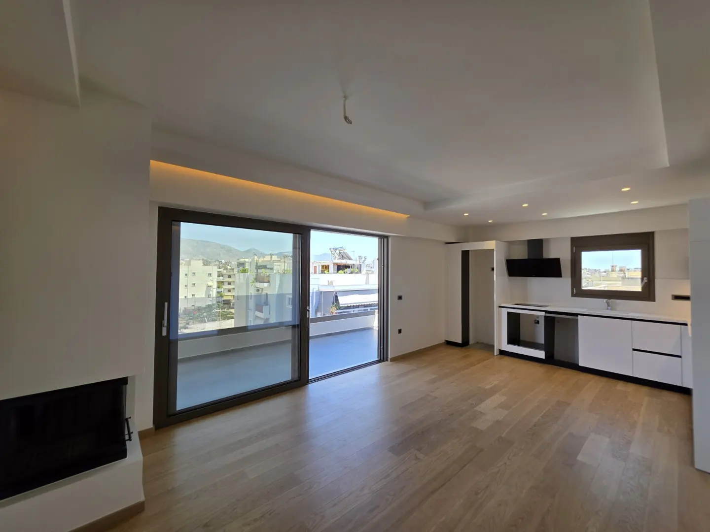 Modern open-plan living area with hardwood floors, a sleek white kitchen, fireplace, and large sliding doors to a balcony.