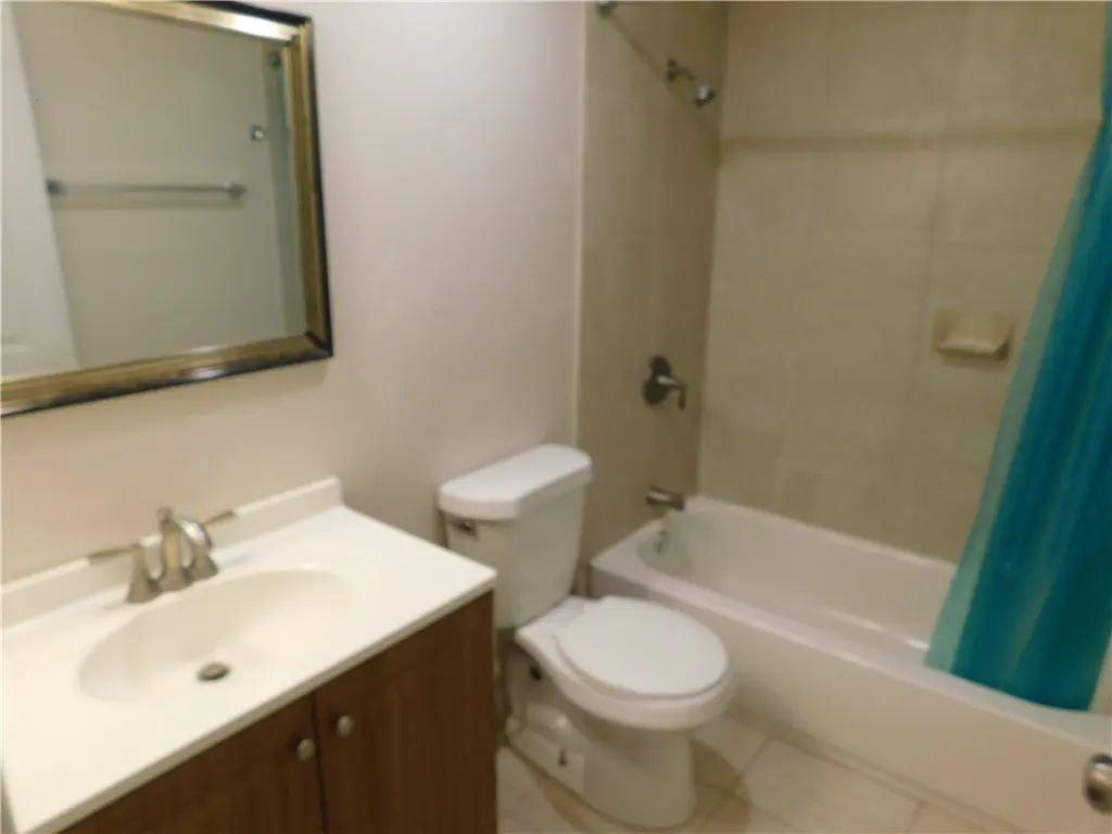 Bathroom with a white toilet, a white sink with a brown cabinet, and a white bathtub with a blue shower curtain.