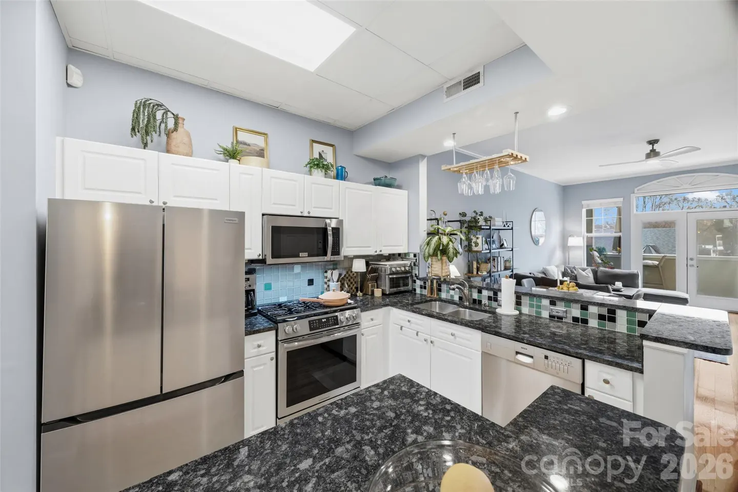 Modern kitchen with white cabinets, stainless steel appliances, dark granite countertops, and an open view to the living room.