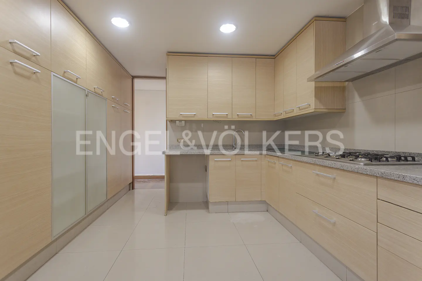 Bright kitchen with light wood cabinets, stainless steel hood, and white tile floor. Engel & Völkers logo visible.
