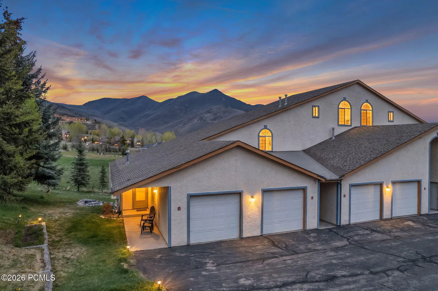 Exterior of a multi-unit home with white garage doors and a mountain backdrop at sunset.