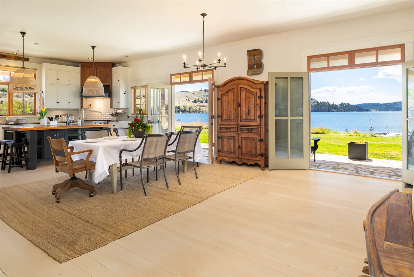 Bright, open kitchen and dining area with lake view. Table set for six, wood cabinet, and open French doors to the outside.