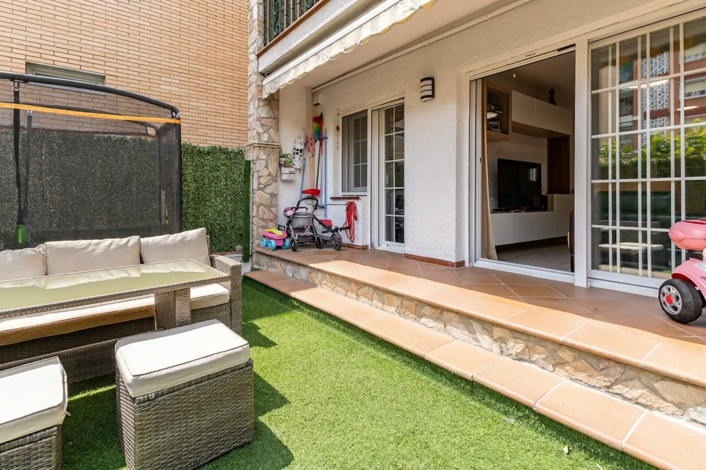 A patio with a wicker sofa set, artificial grass, and a white house with sliding glass doors.