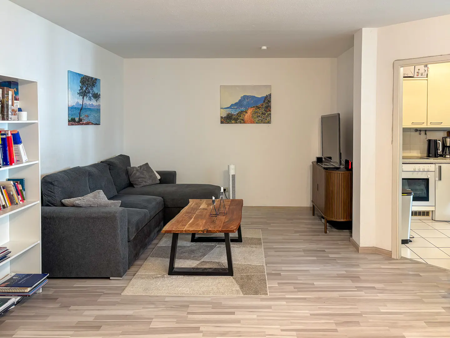 Living room with a grey sectional sofa, live-edge wood coffee table, area rug, and view into a kitchen with white cabinets.