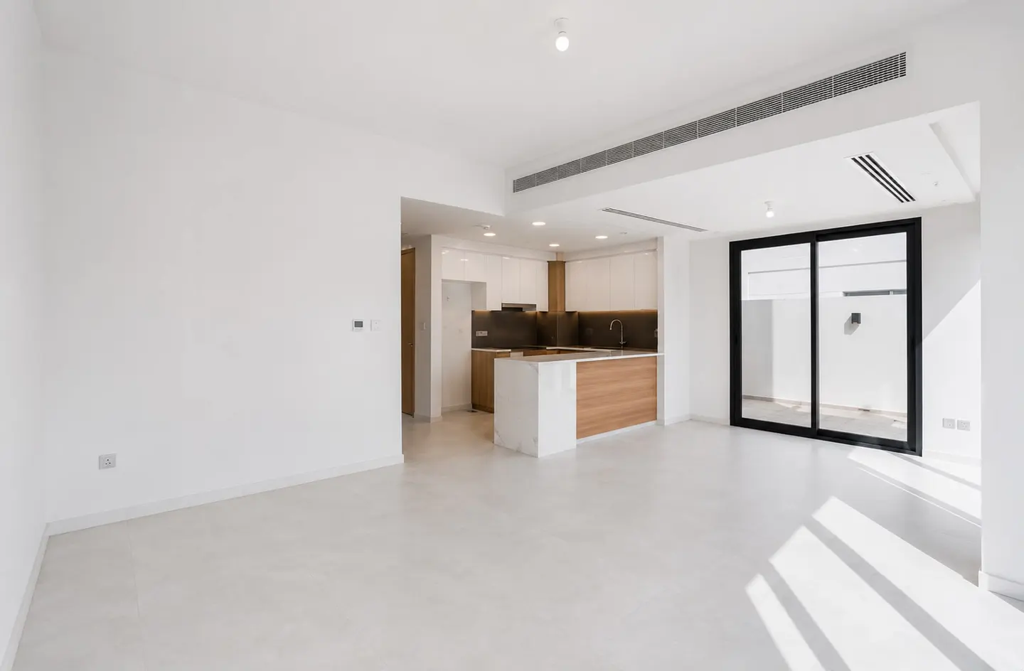 Modern open-plan living area with white walls, light flooring, and a kitchen featuring wood cabinets and a marble island.