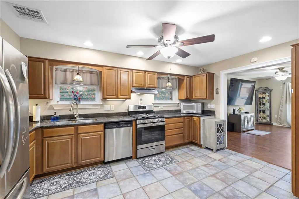 A kitchen with wood cabinets, stainless steel appliances, and tile floors. A ceiling fan is visible.