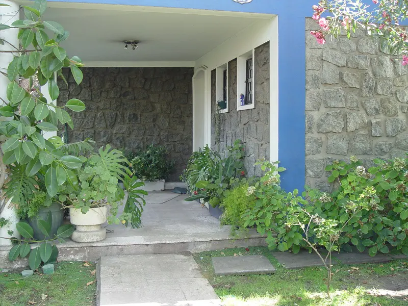 Stone house exterior with blue accents, a covered porch, and lush greenery. Windows are visible.